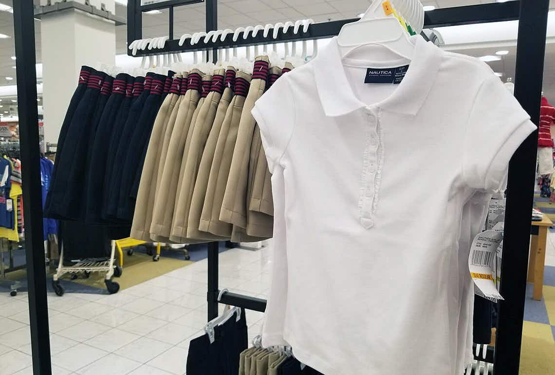 A collared uniform shirt and black and khaki uniform bottoms hanging on a rack inside Macy's.