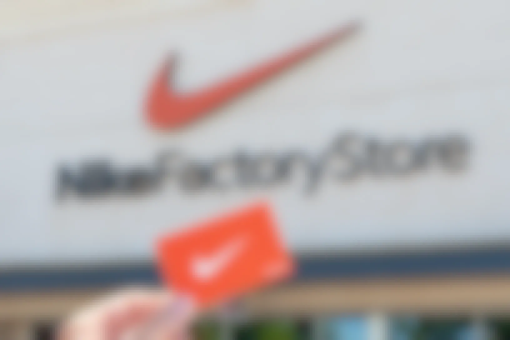 hand holds nike loyalty card in front of nike factory store to get cheap nike gear
