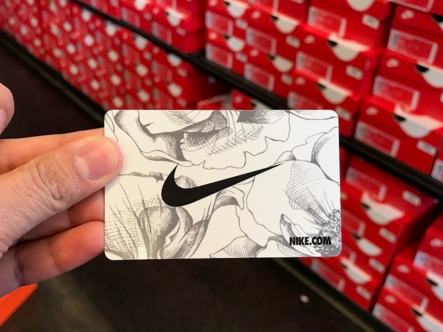 A person holding up a Nike gift card in the shoe aisle of a Nike store