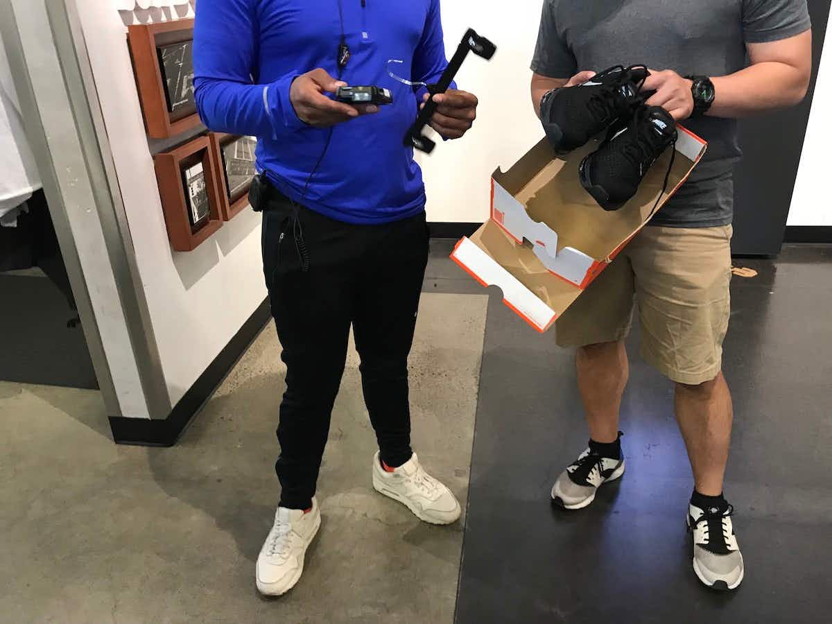 A Nike Factory employee helping a customer who is holding a pair of Nike shoes and a shoe box.