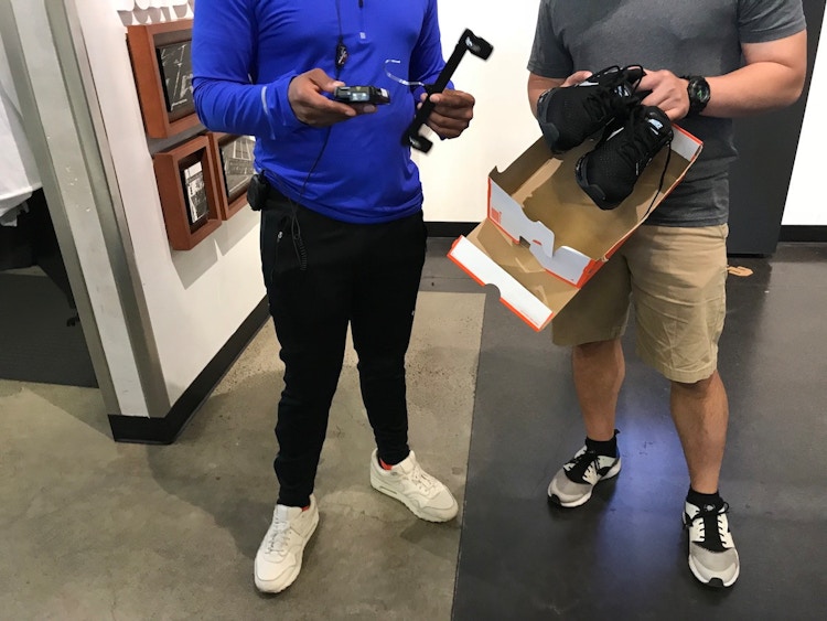 A Nike Factory employee helping a customer who is holding a pair of Nike shoes and a shoe box.
