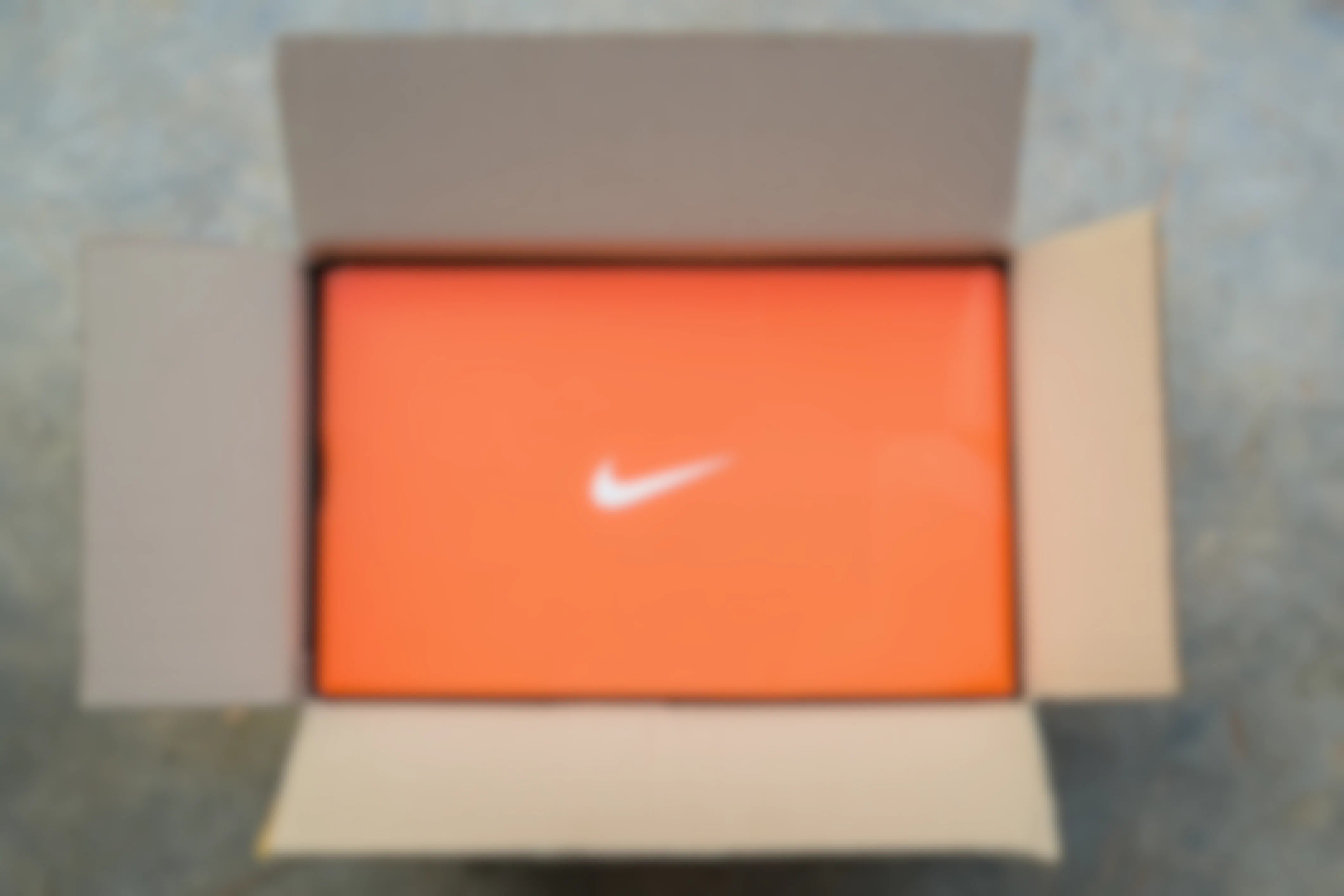 A cardboard box open on the floor with an orange nike shoe box inside.
