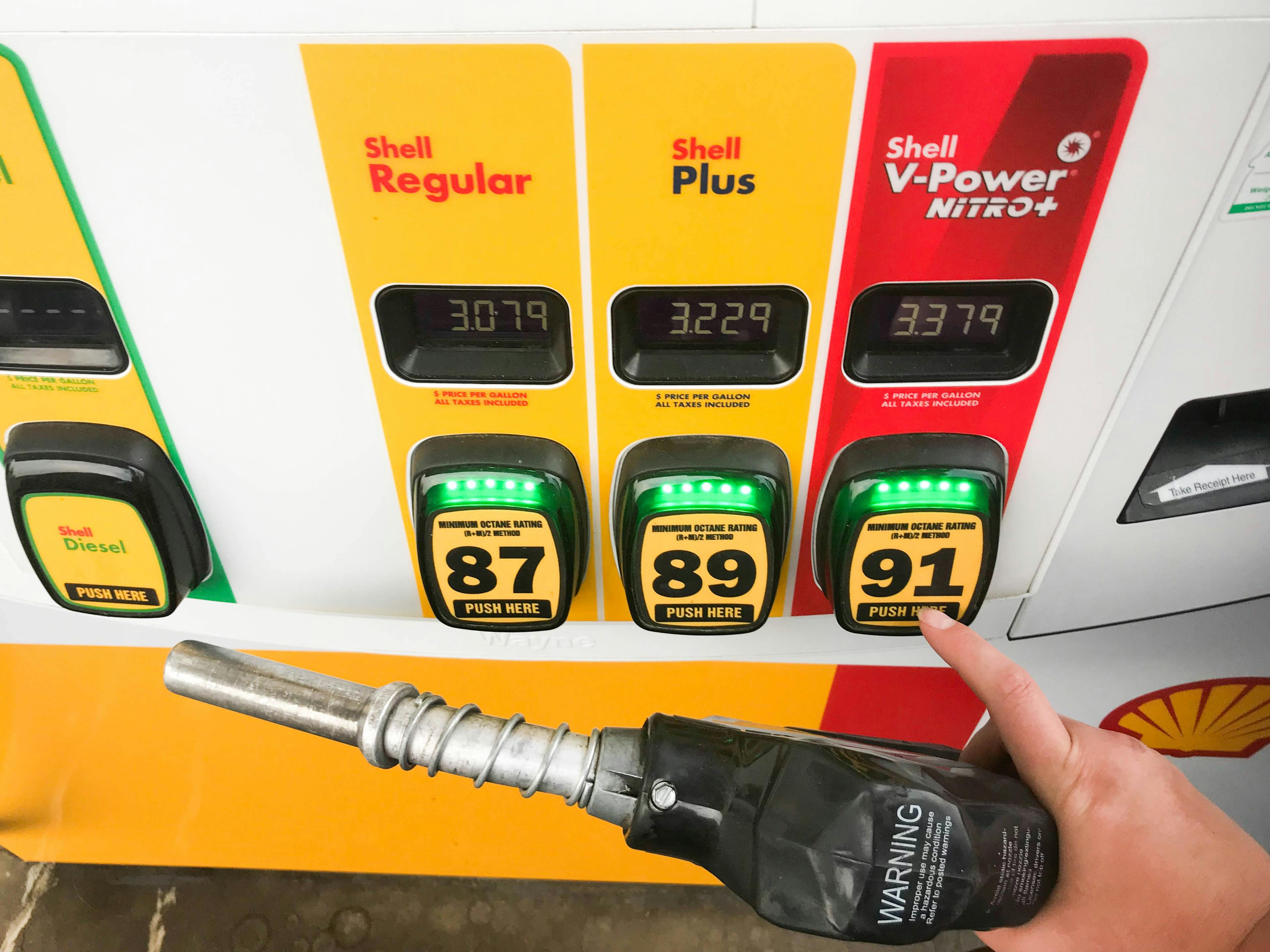 A person's hand holding a gas pump nozzle and choosing their type of gas at a Shell gas station.