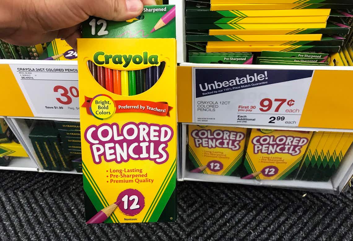 A person's hand holding up a 12 count box of Crayola Colored pencils in front of a shelf with a sale sign that reads, "Unbeatable! $0.97 each