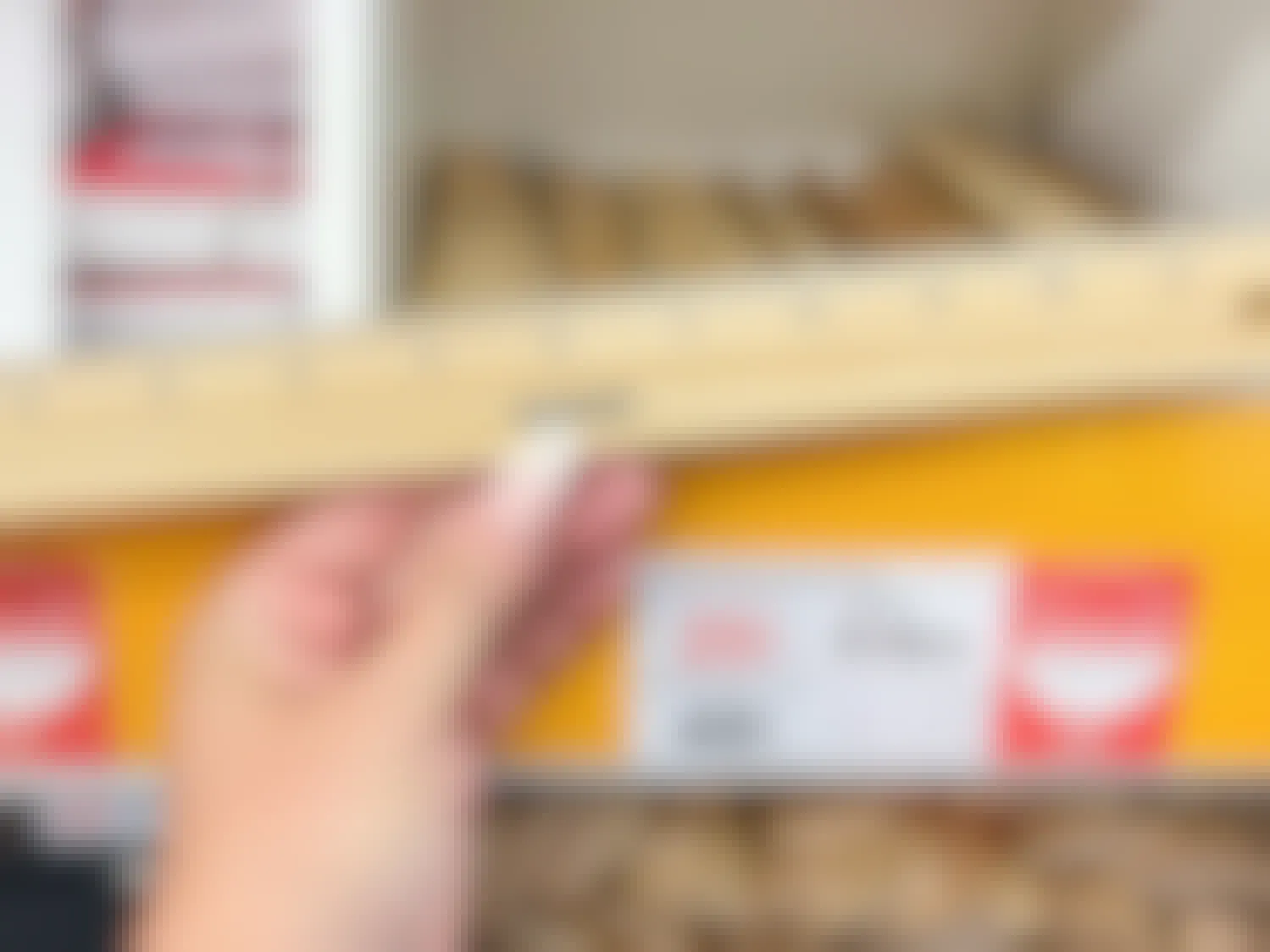 A person's hand holding a Staples ruler in front of a shelf with more rulers on sale for $0.25 at Staples.