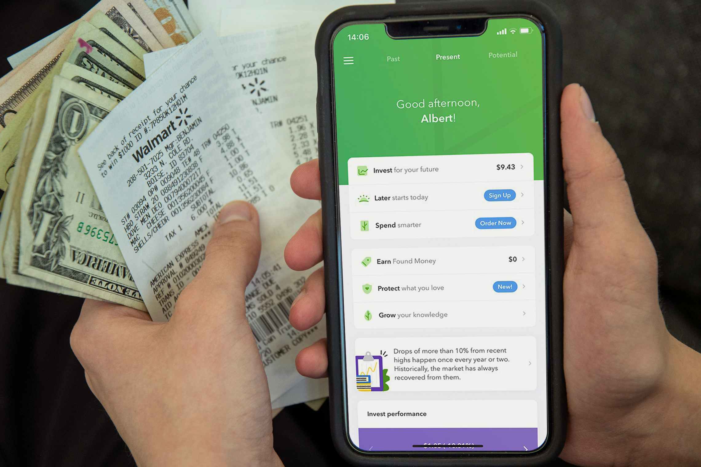 A person holding cash and receipts next to a cell phone displaying the Acorns app.