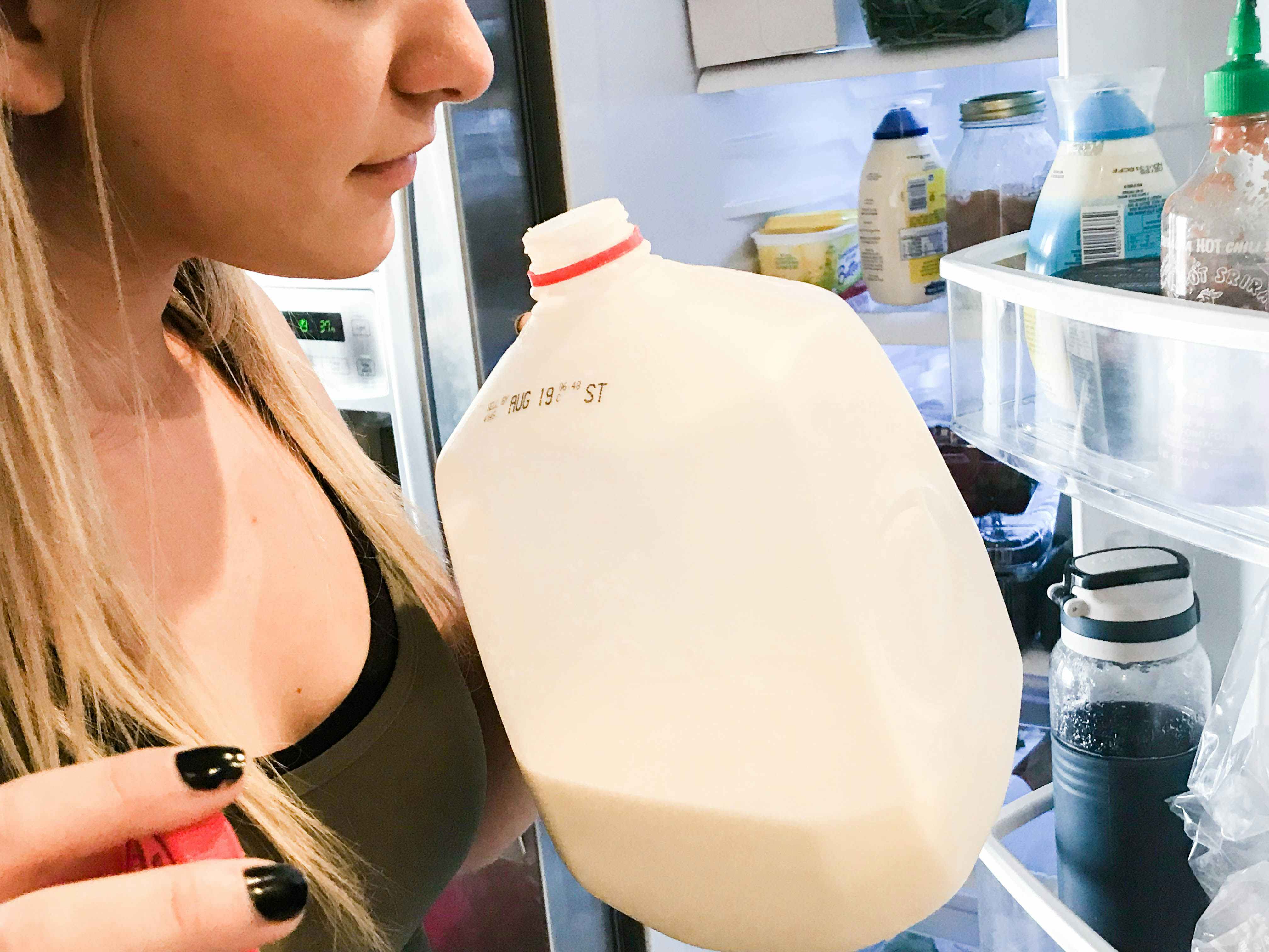 Woman sniffing an open gallon jug of milk.