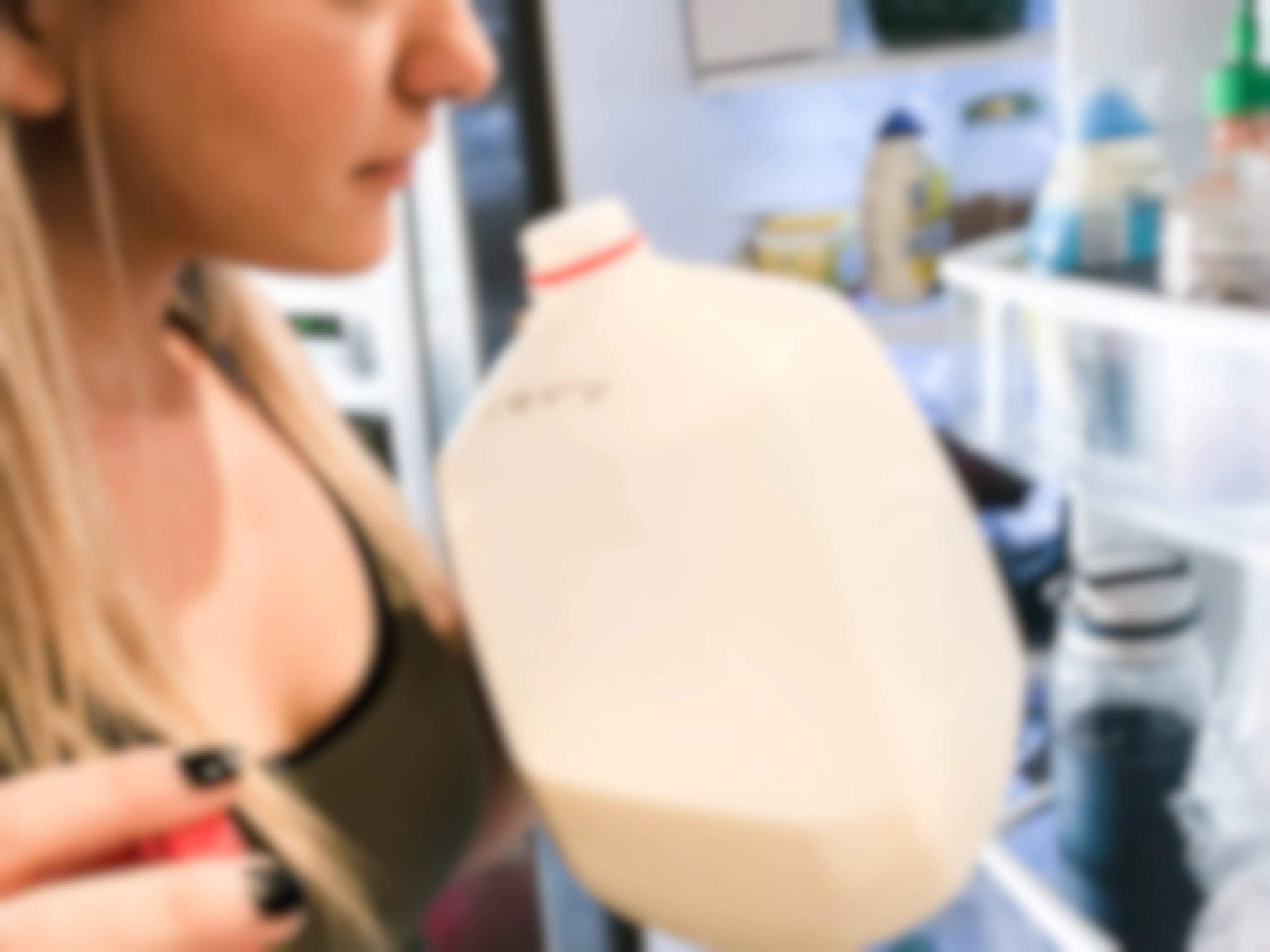 Woman sniffing an open gallon jug of milk.