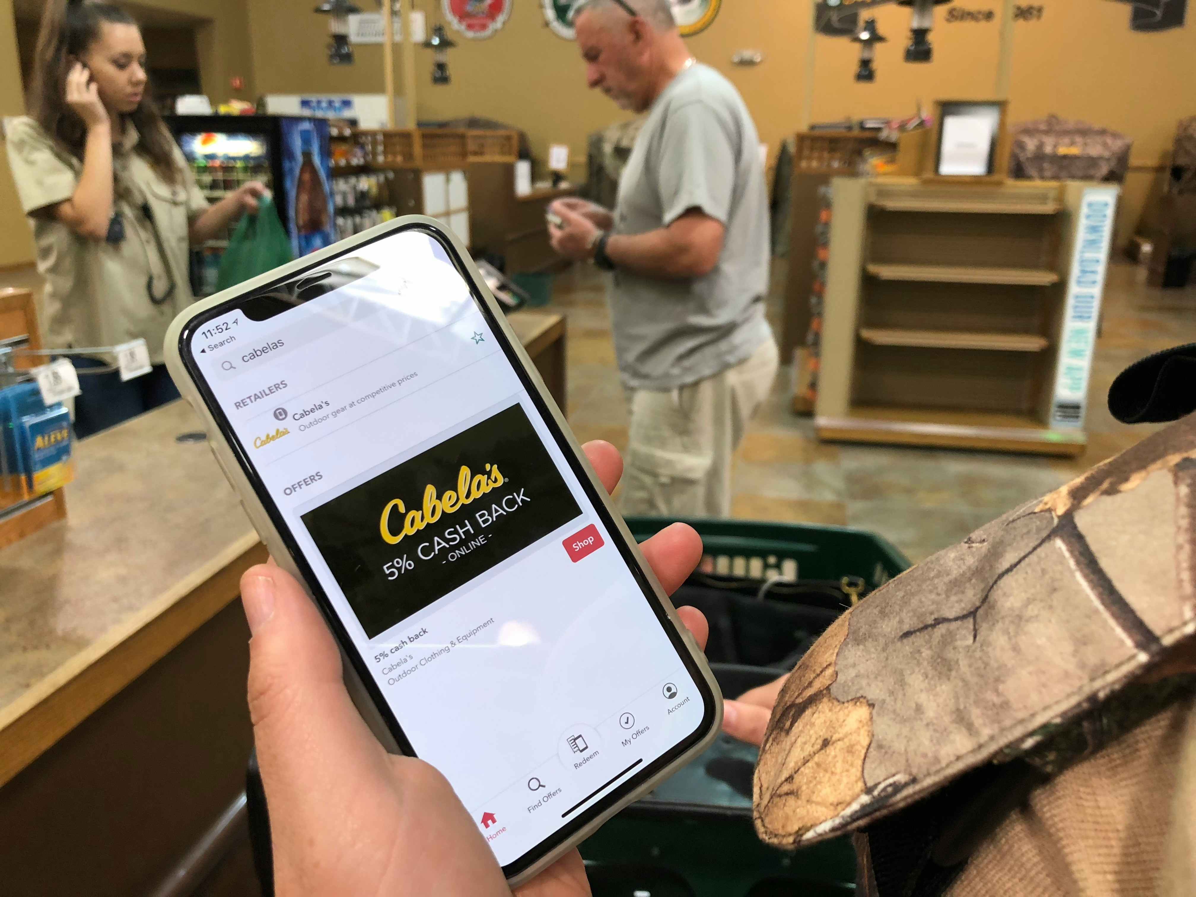 A person's hand holding their phone that is displaying the Cabela's rebate reward on the iBotta app.
