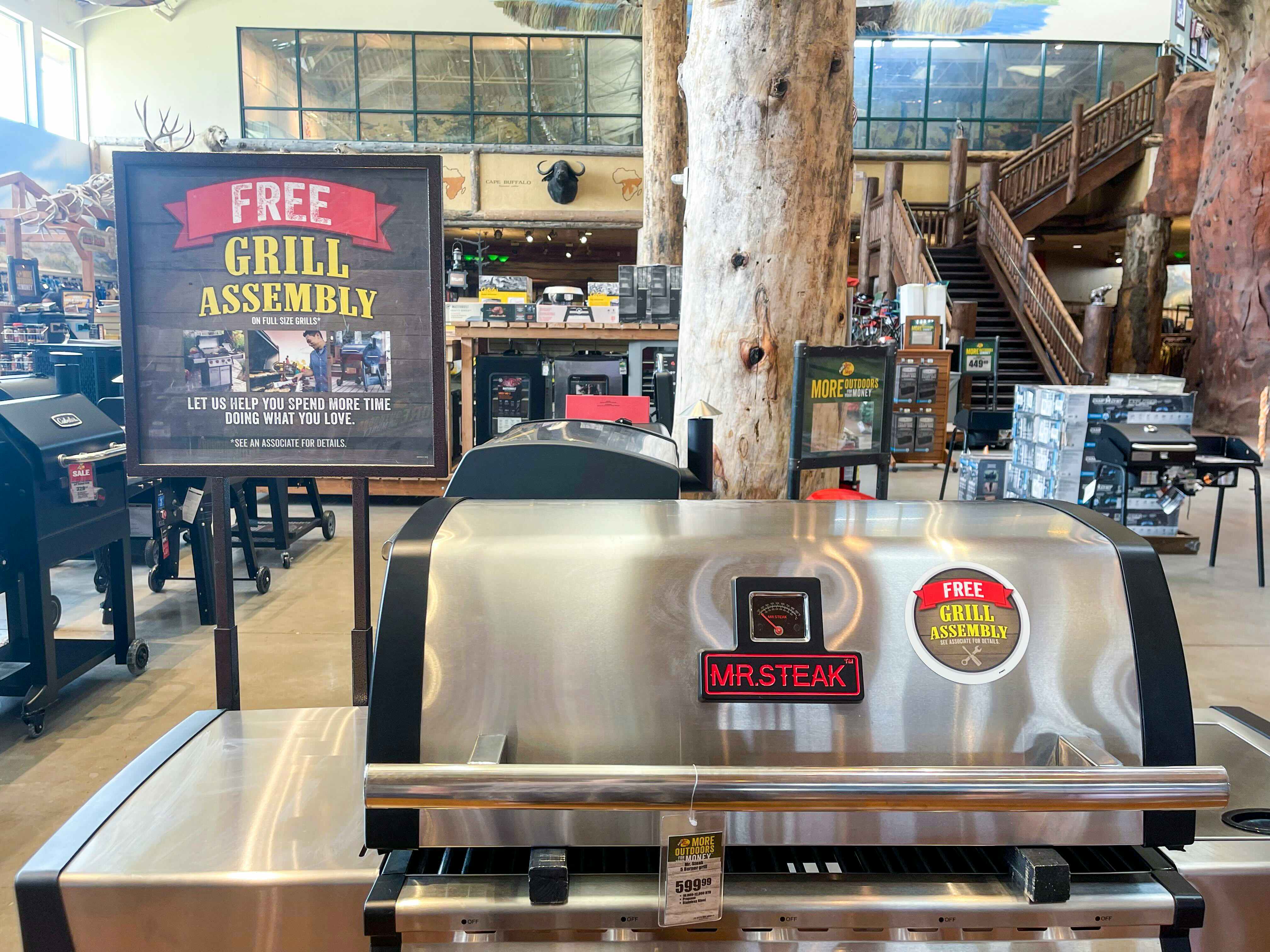 A barbecue grill on display next to a sign that reads, "Free Grill Assembly" inside Cabela's.