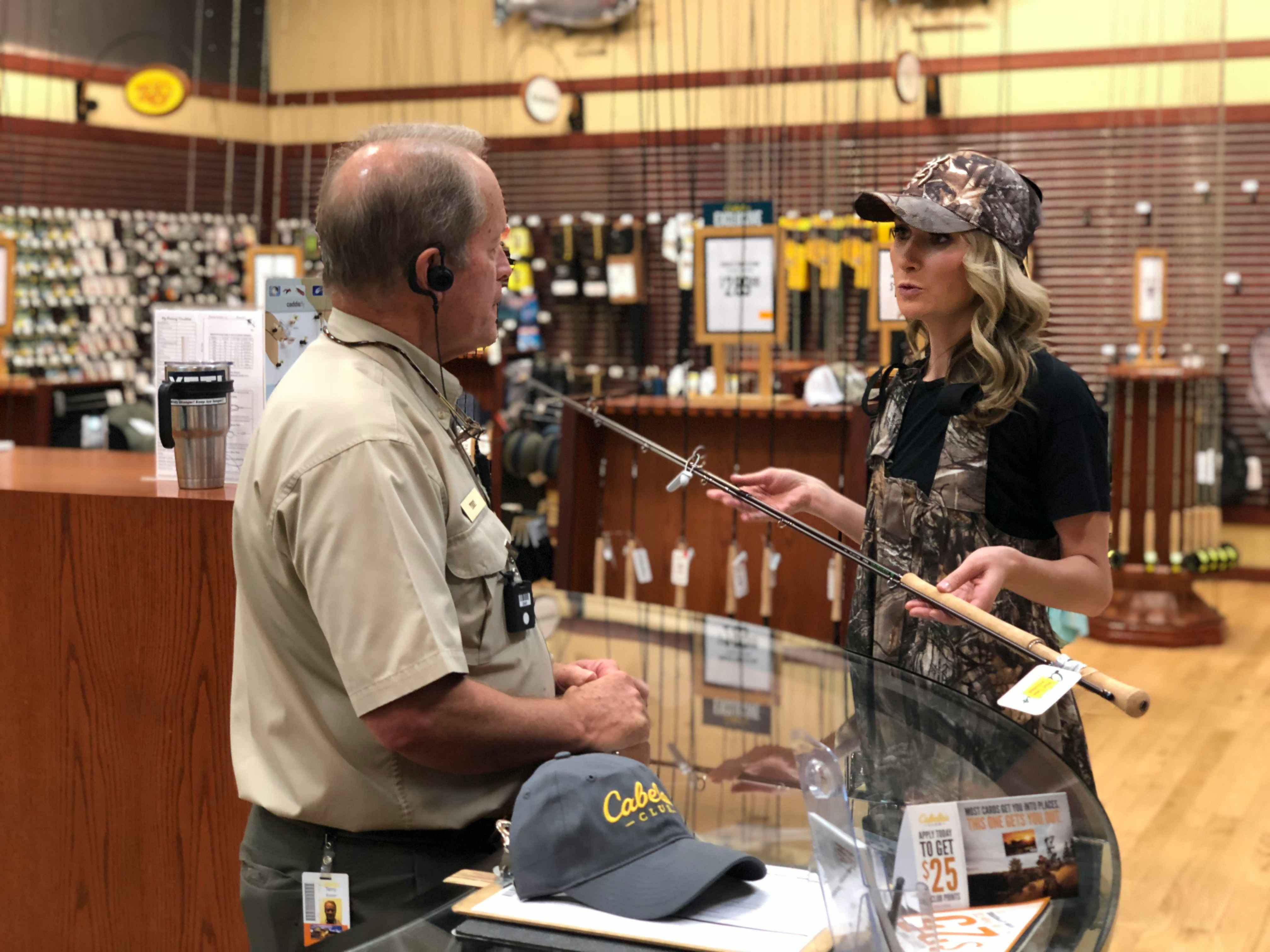 A woman talking to a Cabela's employee while holding a fishing rod.