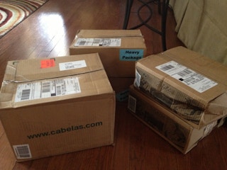 Four unopened packages from Cabelas.com sitting on a living room floor.