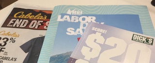 Ad books for Cabela's, REI, and Dick's Sporting Goods laying on a table.