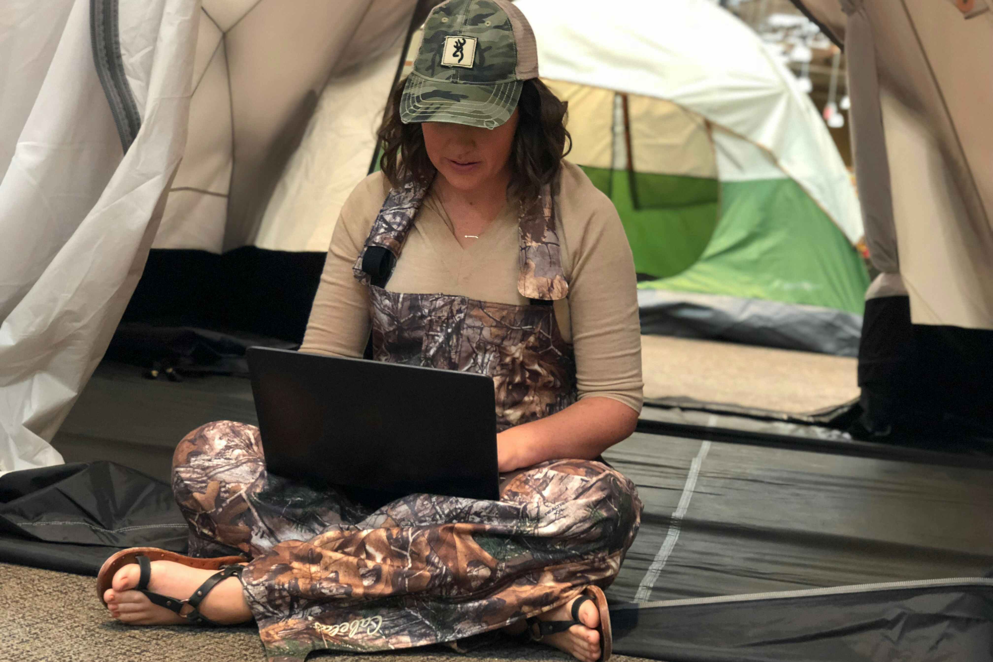 A woman sitting in a tent display inside Cabela's and using a laptop computer.
