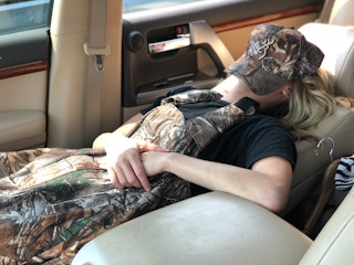 A woman sleeping in a reclined passenger seat with her hat covering her face.