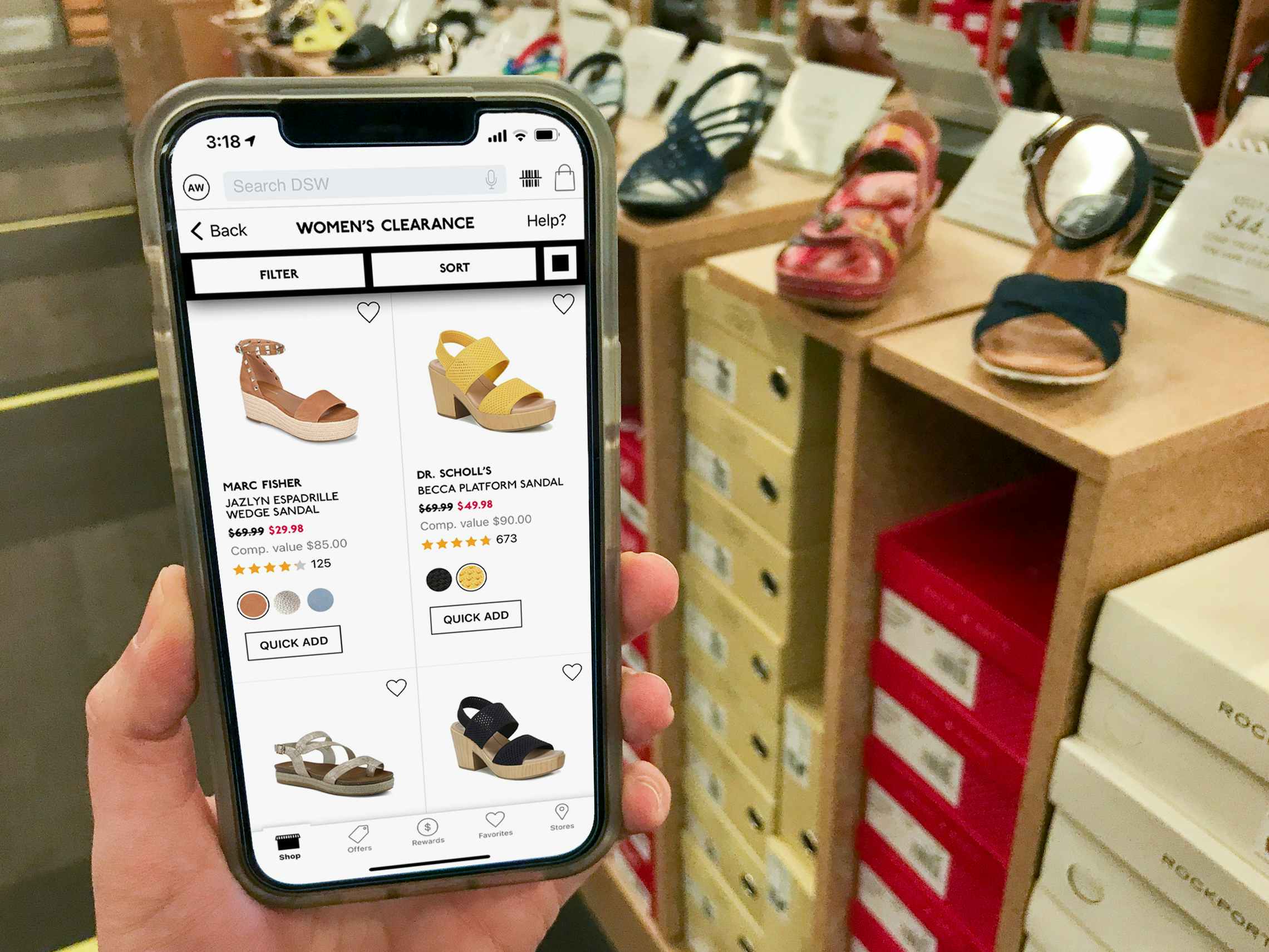 An iPhone displaying the DSW app showing clearance shoes, held next to similar shoes in the store.