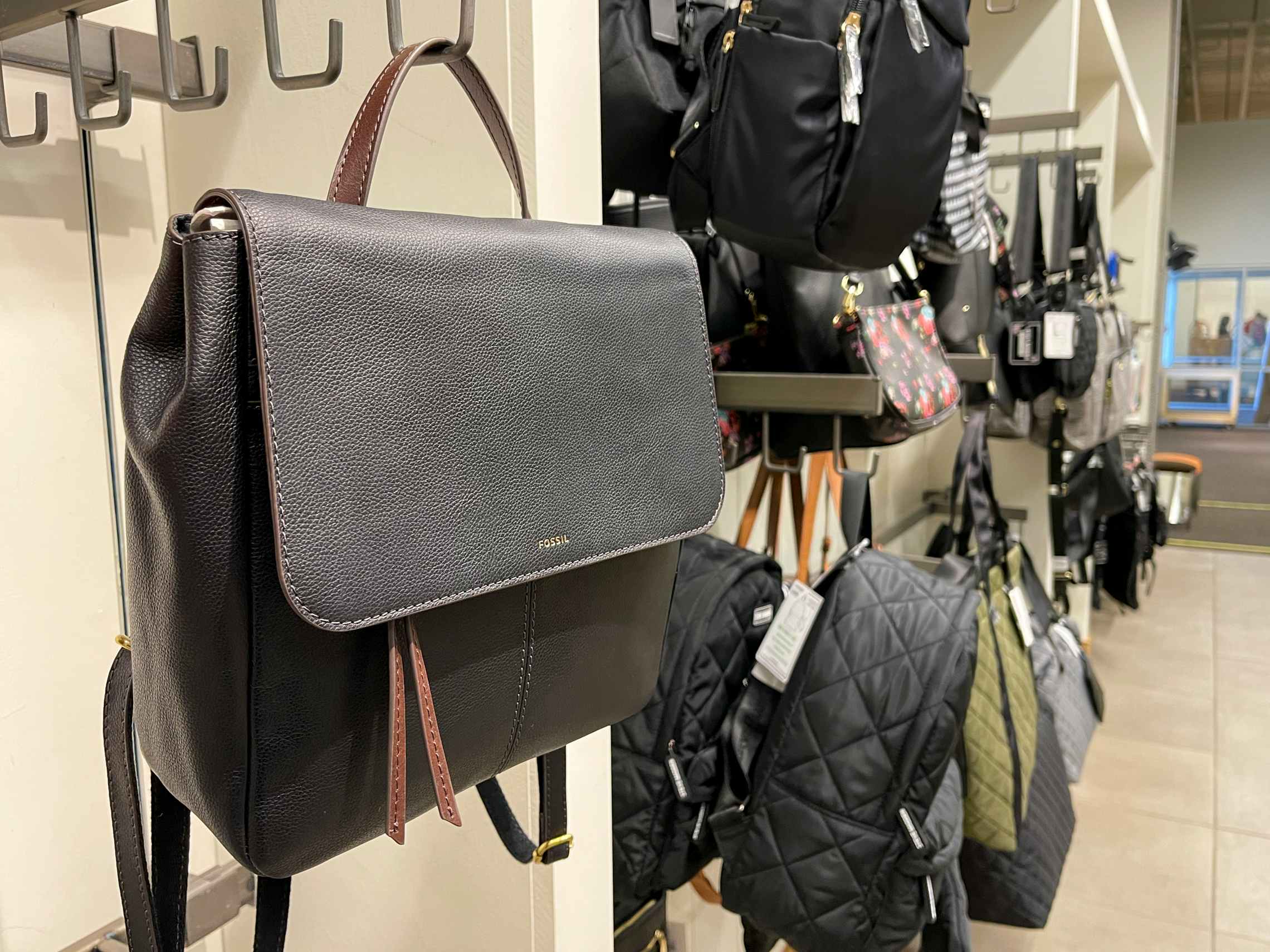 A fossil bag with other purses and backpacks hung on hooks inside a DSW store.