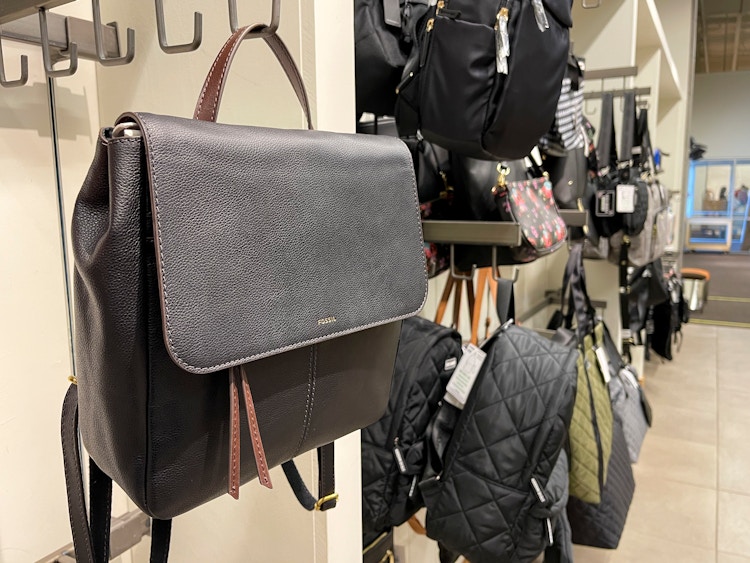 A fossil bag with other purses and backpacks hung on hooks inside a DSW store.