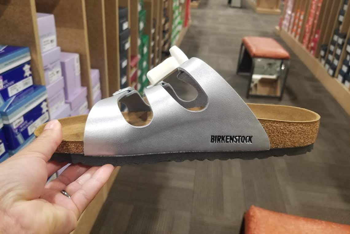 A person's hand holding a Birkenstock sandal in the aisle of a shoe store.