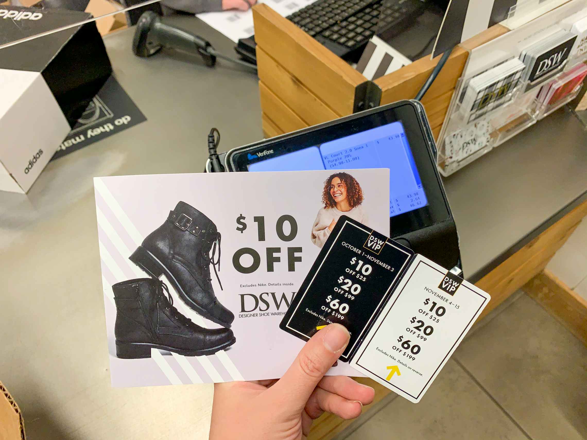 A person holding DSW coupons at the checkout register in store.