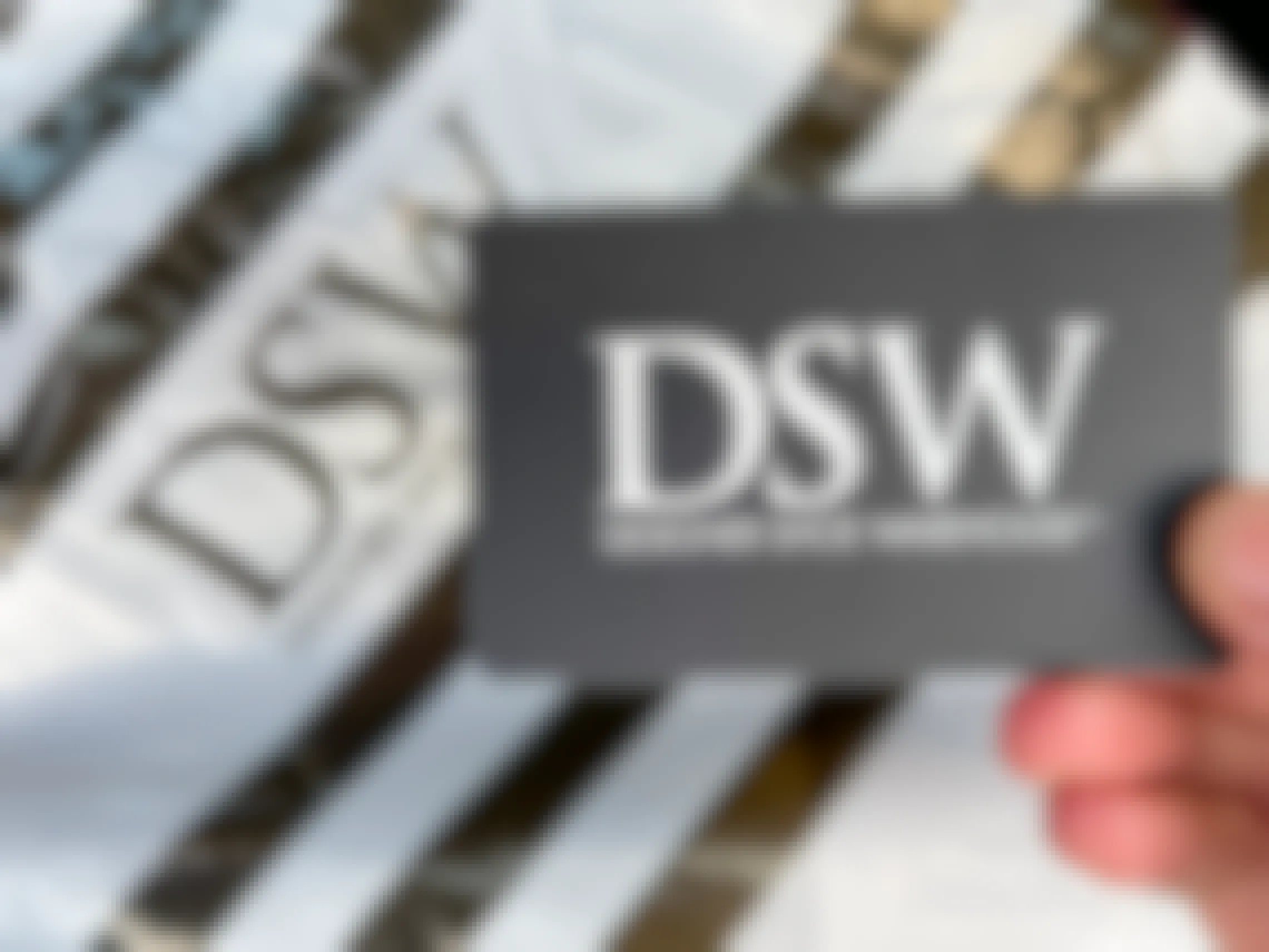 A person holding a DSW gift card next to a DSW shopping bag.