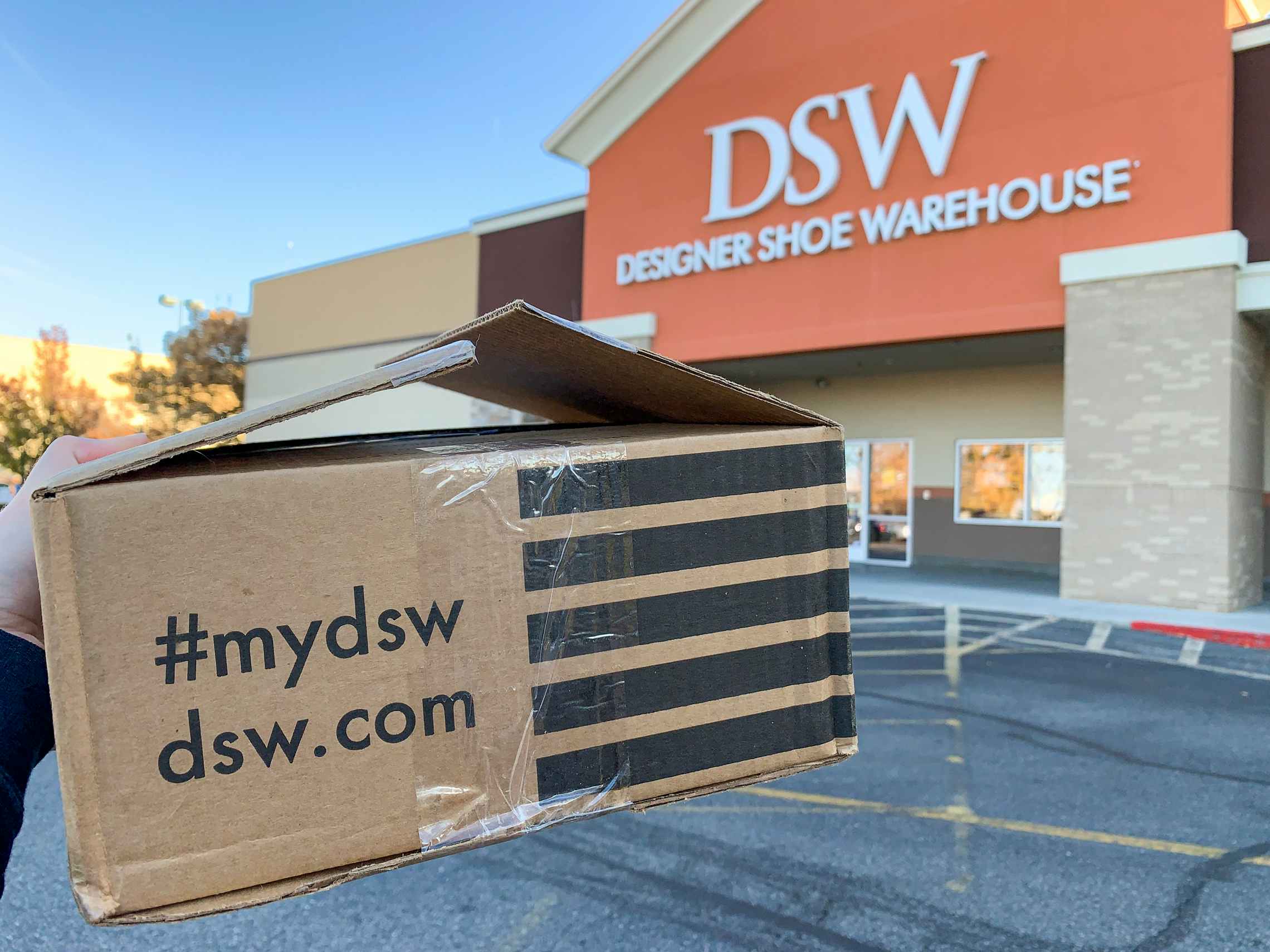 A DSW.com shipping box held in front of a DSW store.