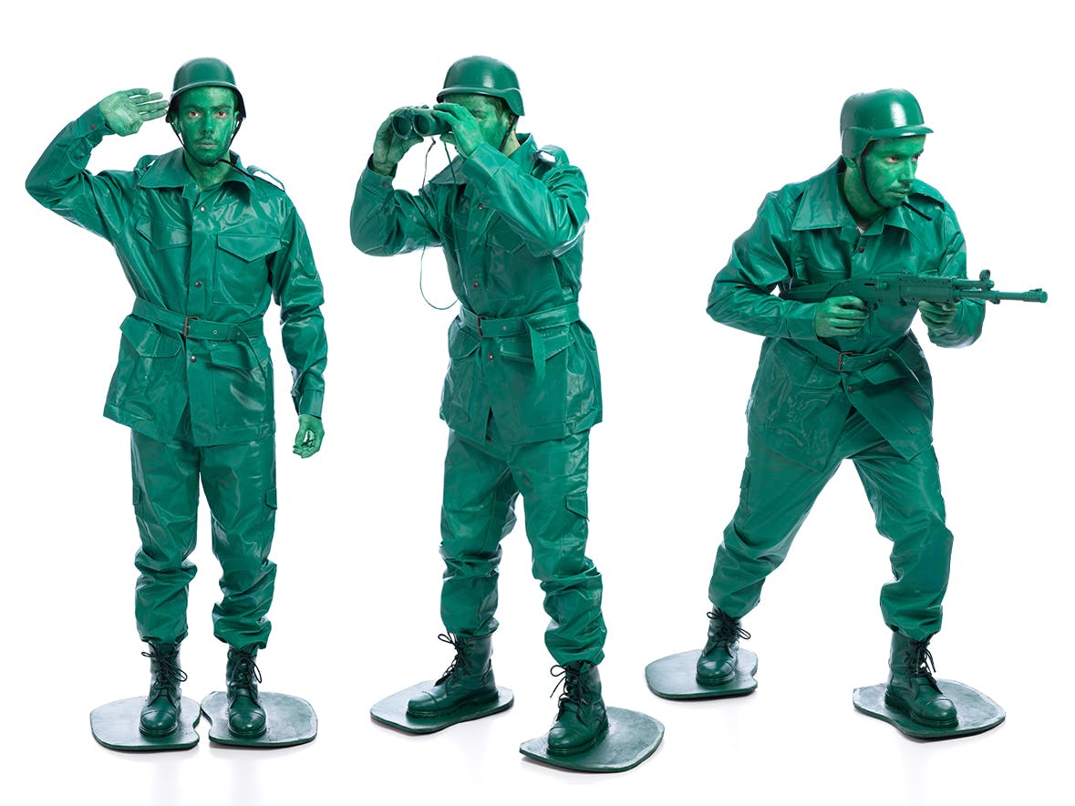 A man dressed as a green plastic army man posing as the toy does in three different positions.