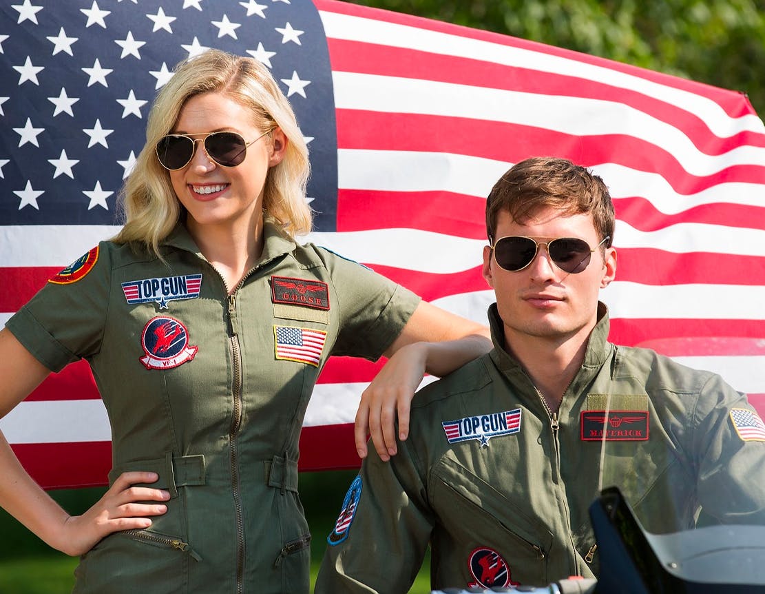 Two people dressed in Top Gun costumes sitting in front of an American flag.