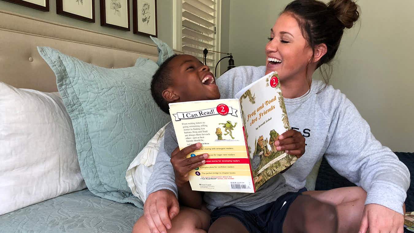 A mom sitting with a child and laughing while reading a book.