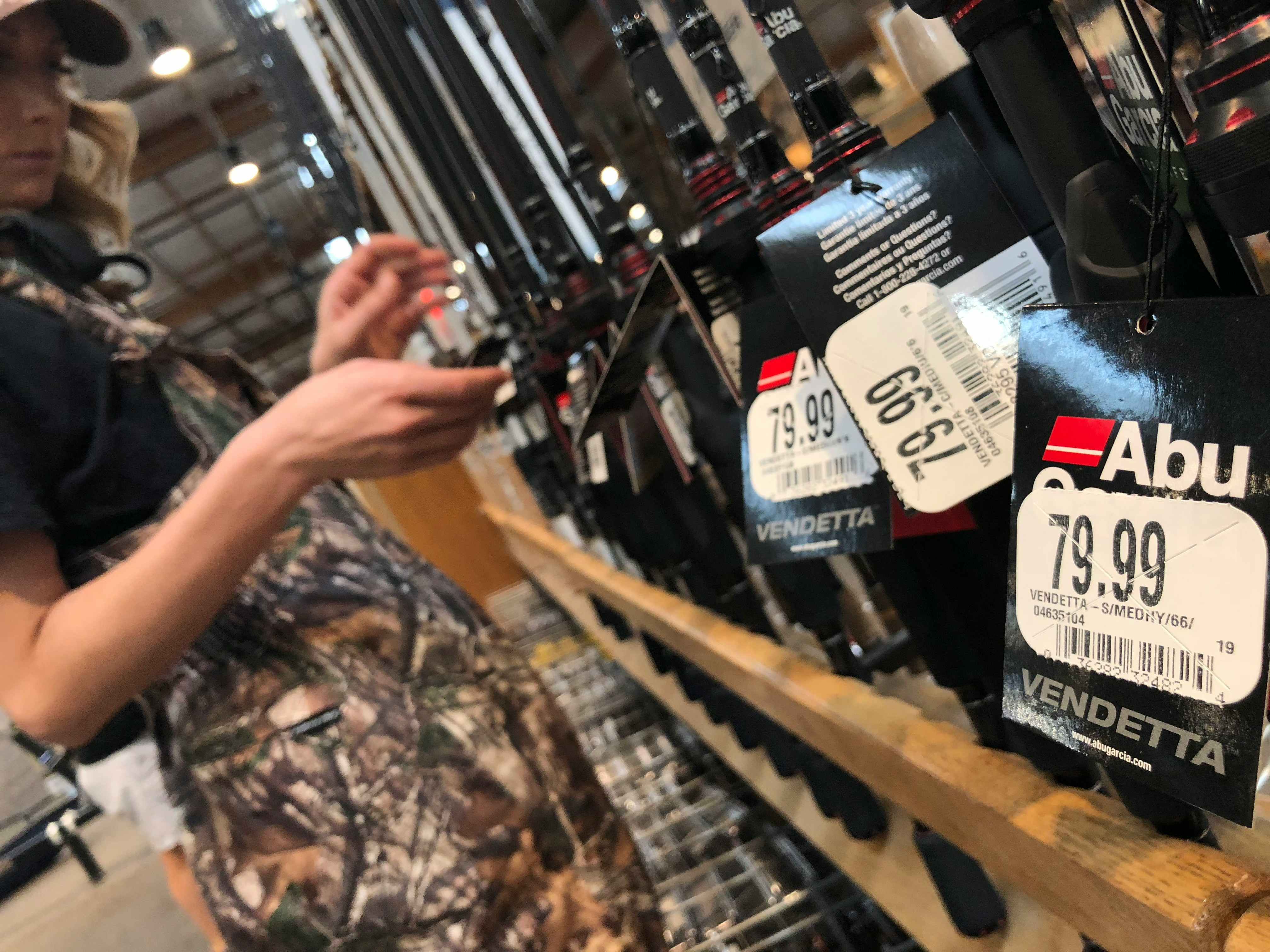 A person looking at fishing rods inside Cabela's, with white price tags in focus.