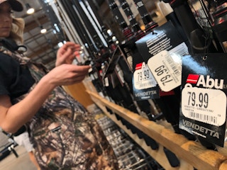 A person looking at fishing rods inside Cabela's, with white price tags in focus.