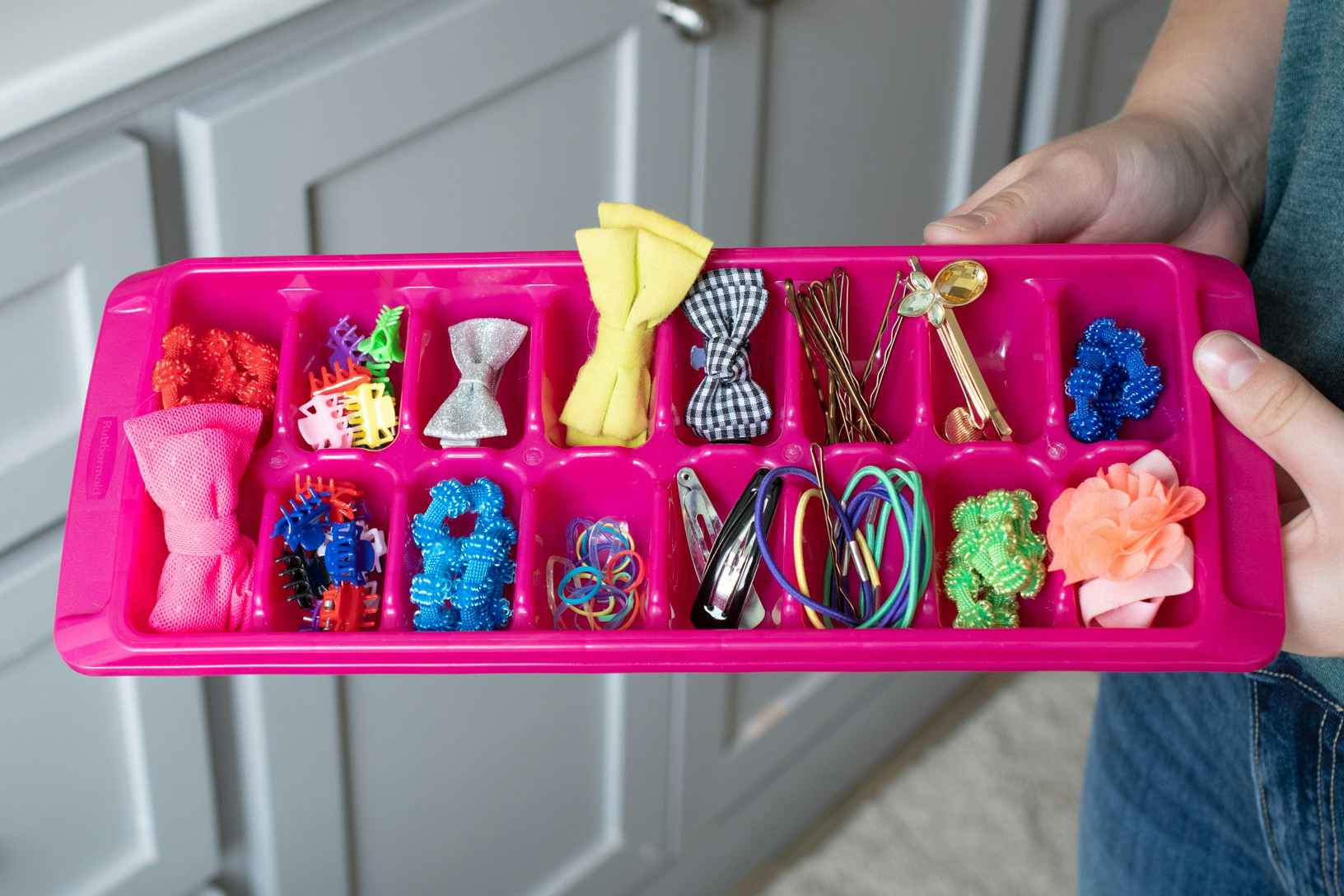 A woman holding an ice cube tray filled with colorful hair accessories.