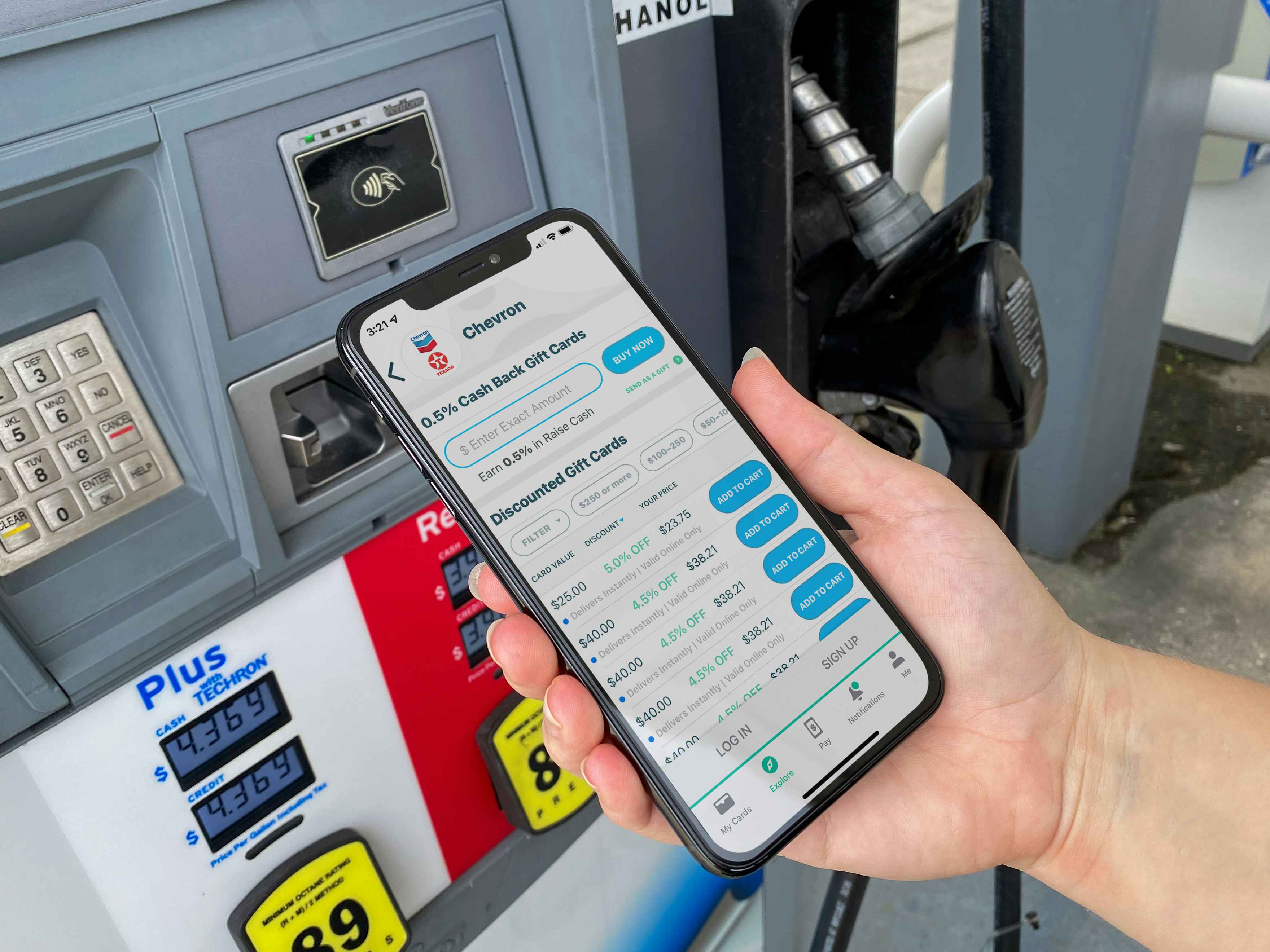A person holding their phone displaying the Raise discount gift card app in front of a gas pump.