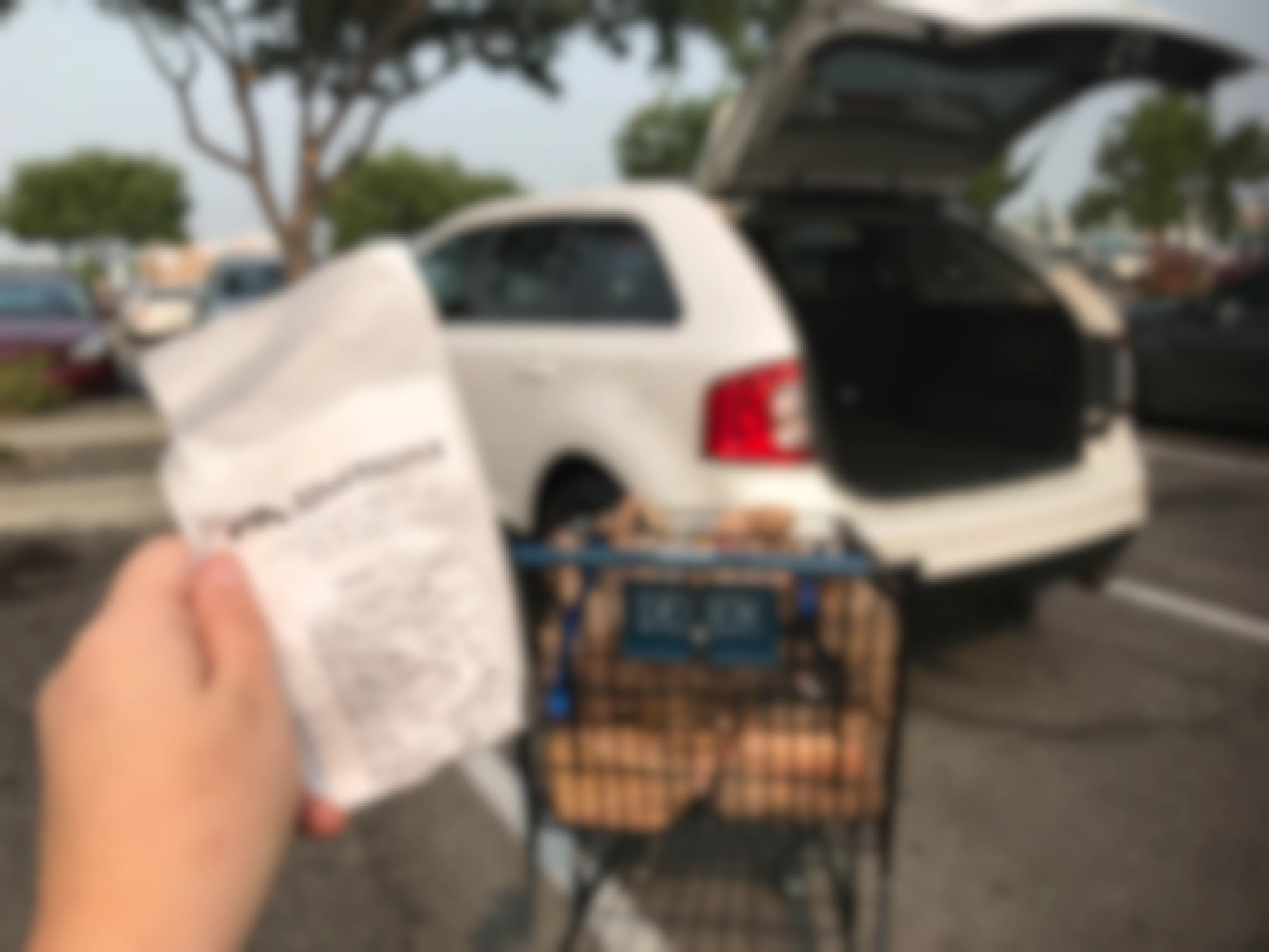hand holds a receipt in front of car with open trunk at an albertsons store