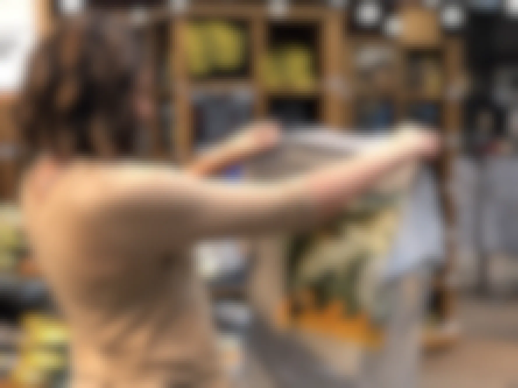 A woman holding up and looking at a Cabela's t-shirt in the clothing section of Cabela's.