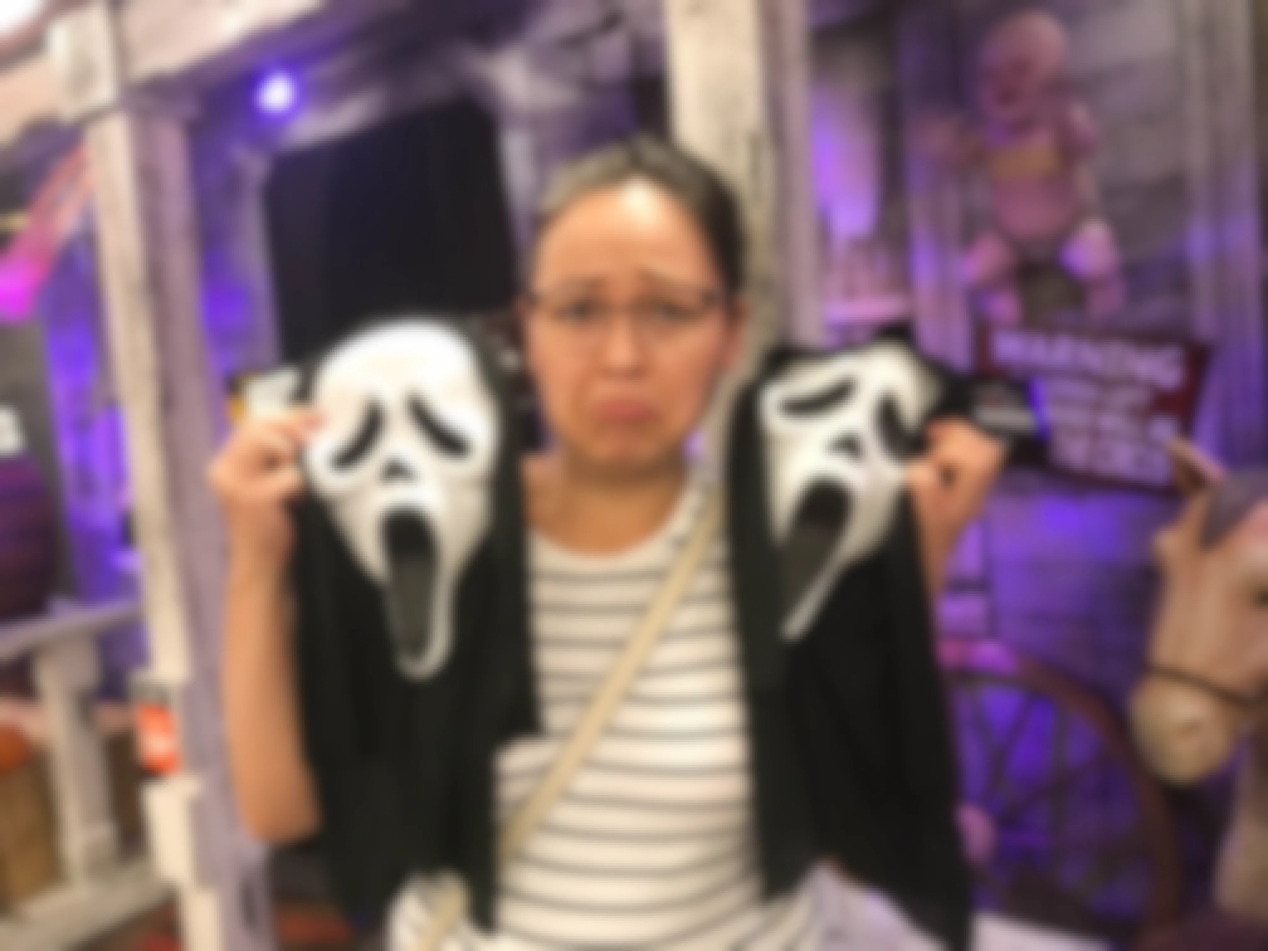 A woman holding up two ghostface masks and frowning