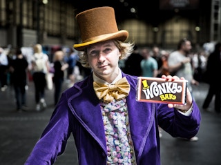 A man dressed as Willy Wonka holding up a chocolate bar.