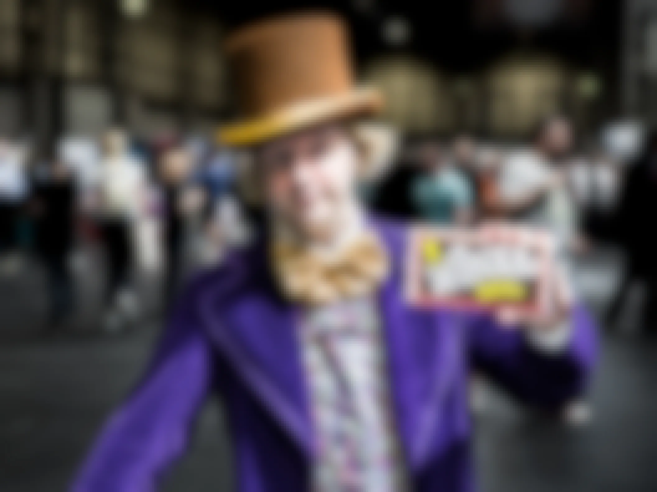 A man dressed as Willy Wonka holding up a chocolate bar.
