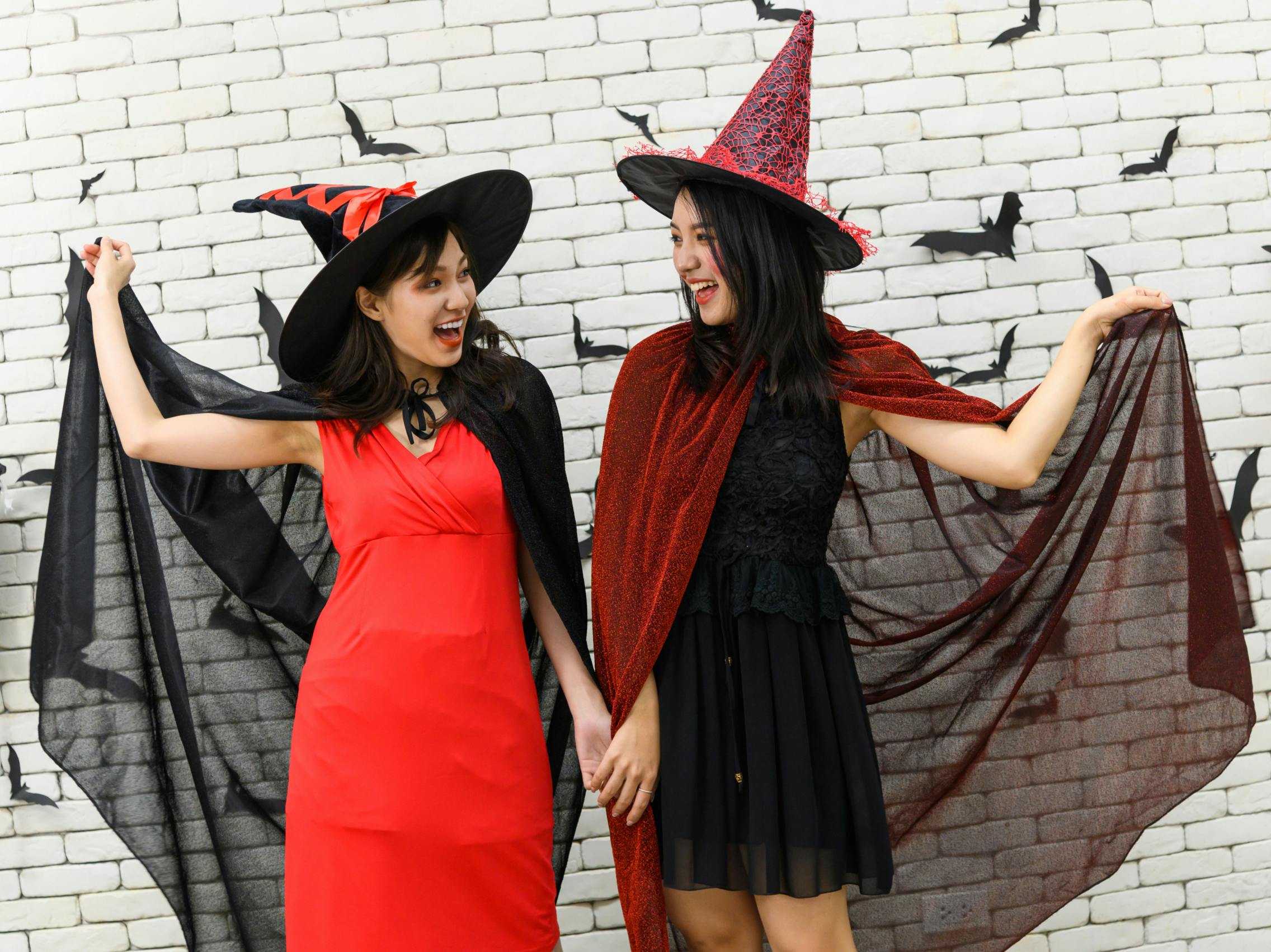 Two women dressed as witches smiling at each other in front of a white brick wall.