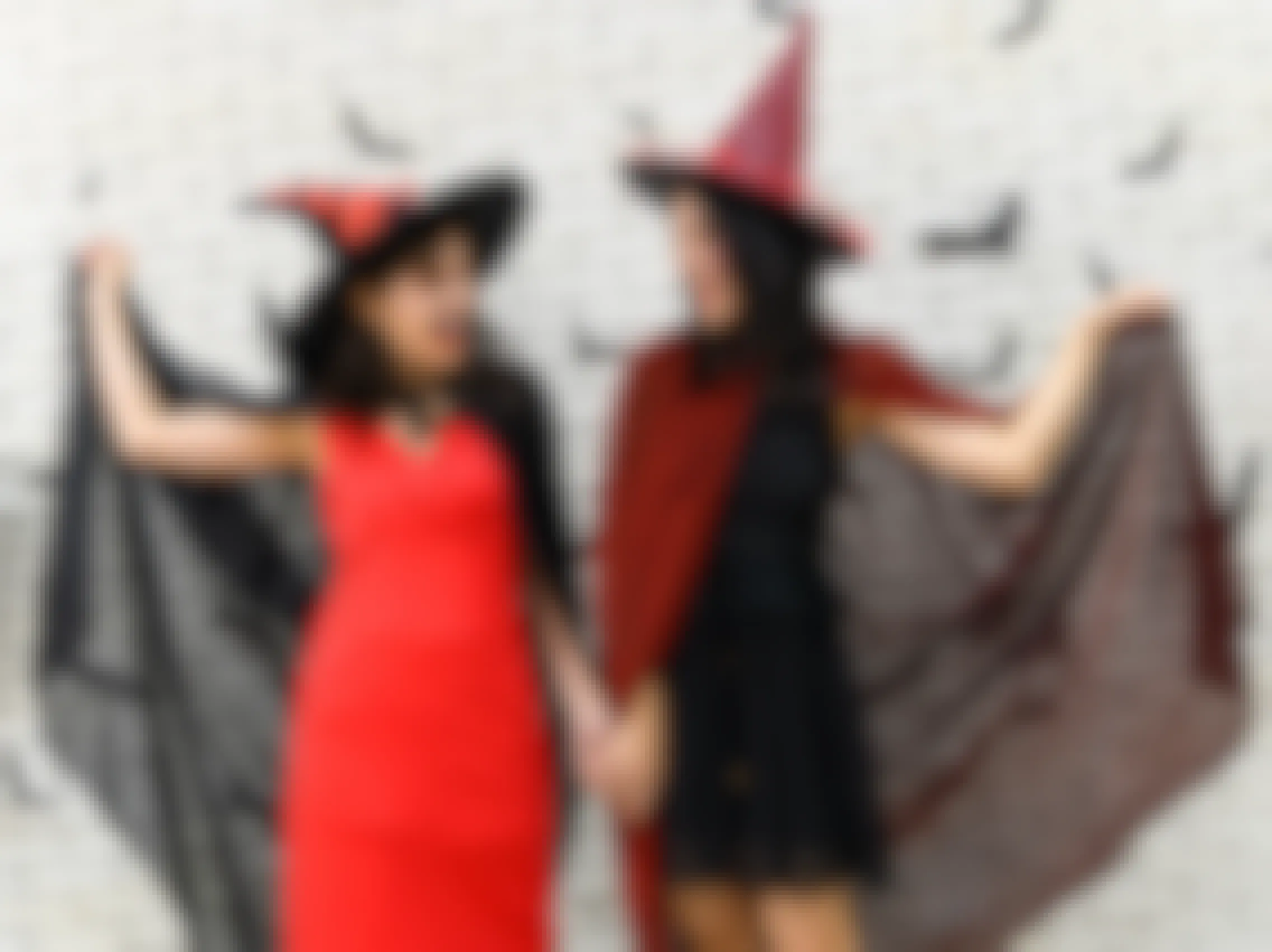 Two women dressed as witches smiling at each other in front of a white brick wall.