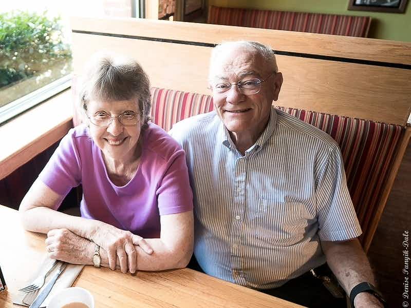 Two senior people sitting in a booth at Applebee's, smiling at the camera.