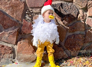A little boy dressed as a chicken for Halloween standing against a stone wall