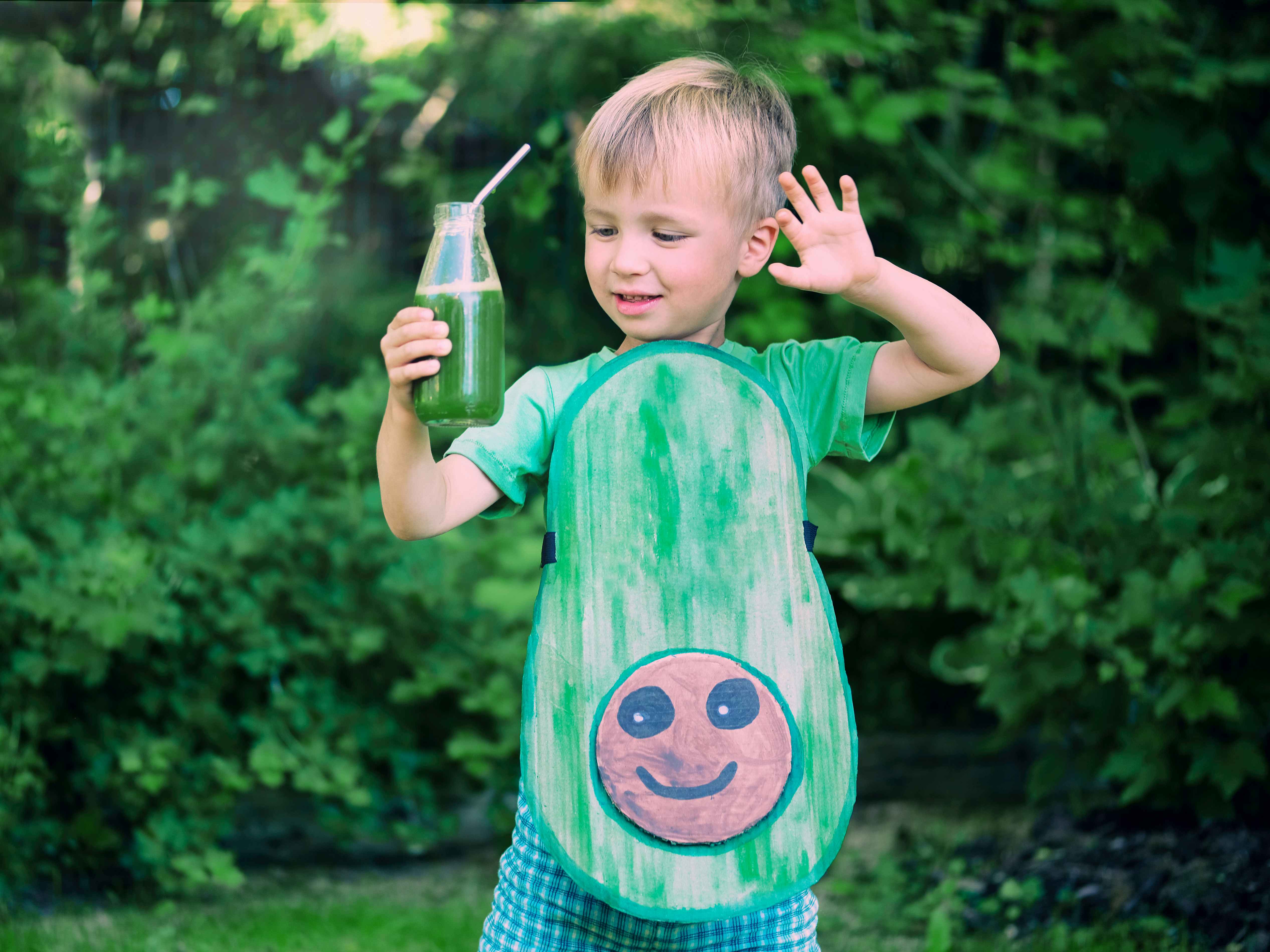 A child dressed up as aa avocado holding a drink with a bendy straw in it.