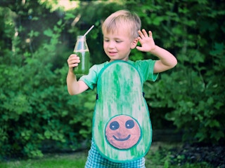 A child dressed up as aa avocado holding a drink with a bendy straw in it.