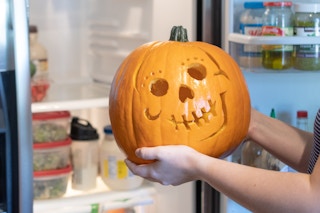 Someone putting a carved pumpkin into a refrigerator