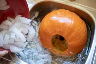 A pumpkin being placed in a sink full of ice