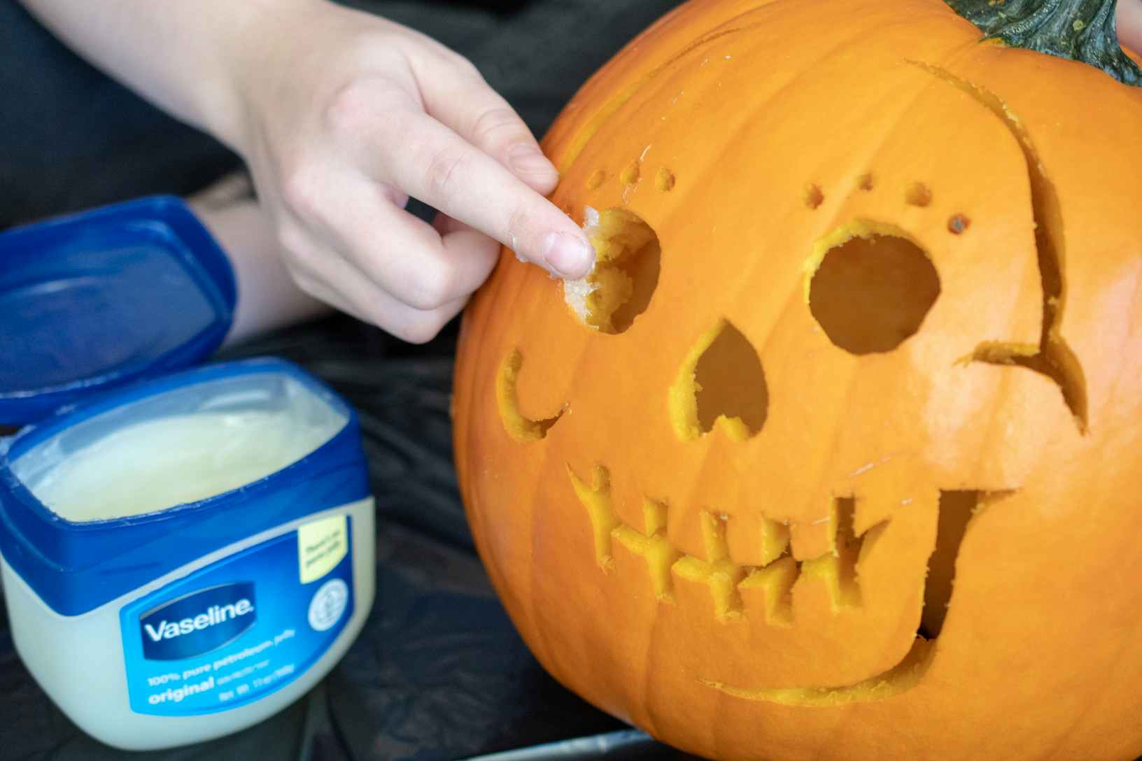 Person applying vaseline to a carved pumpkin