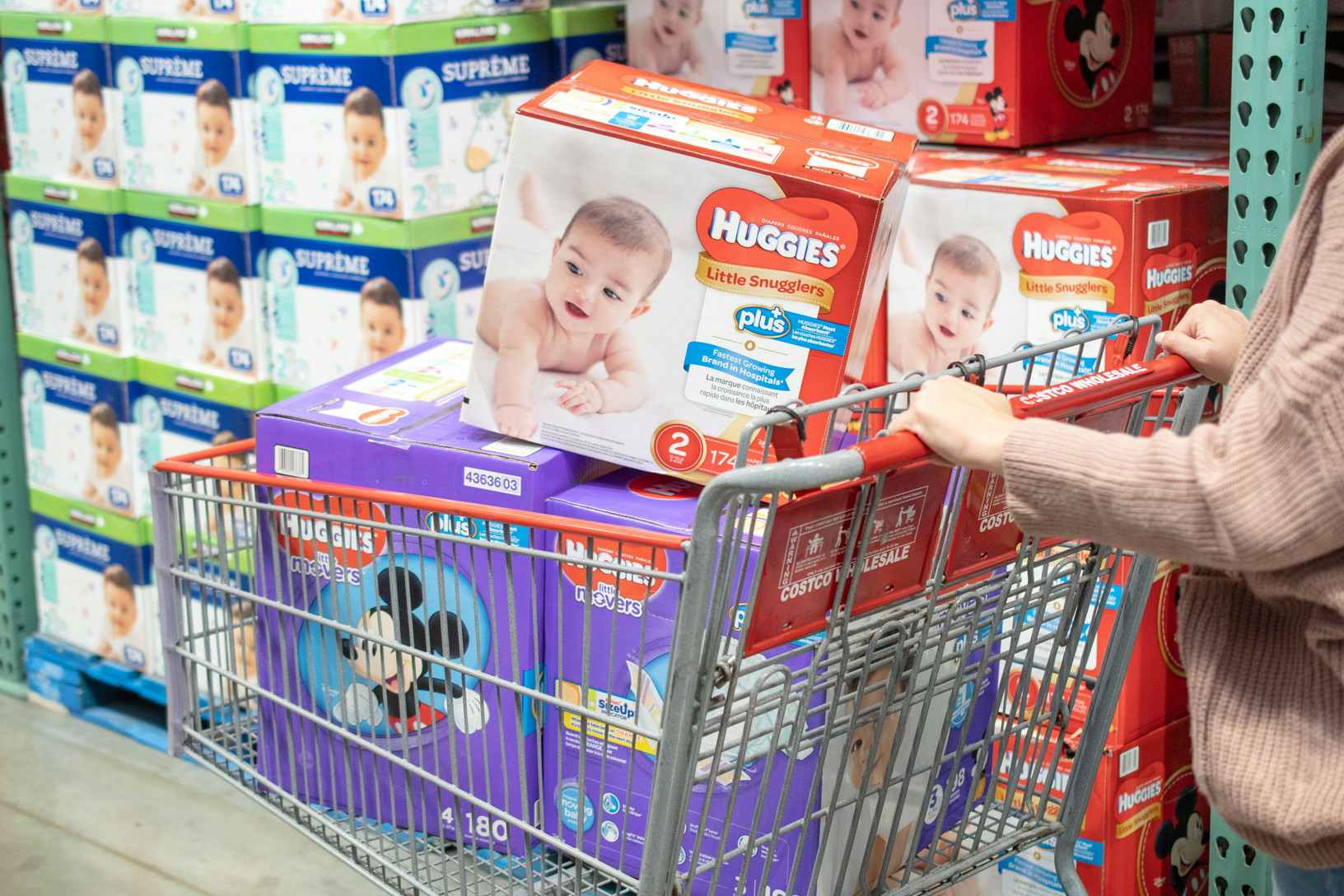 person pushing grocery cart with three boxes of Huggies diapers
