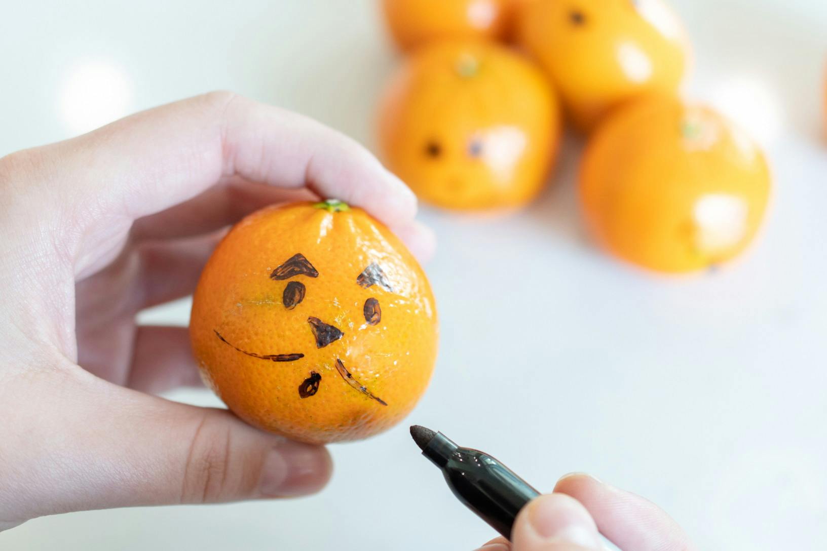 A person drawing a face on an cutie orange.