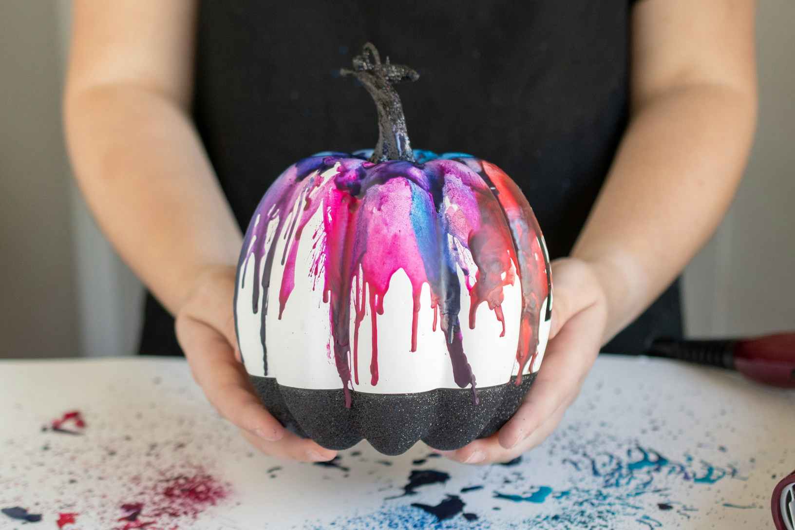 person holding pumpkin decorated with melted crayons
